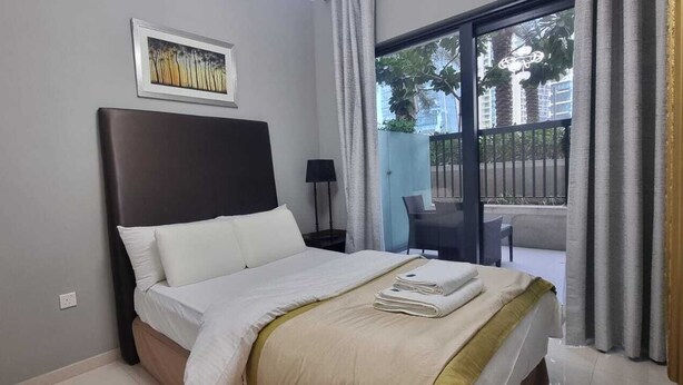 Ein Hotelzimmer mit einem Bett, einem gerahmten Bild an der Wand, einem Fenster mit Vorhängen und einem Stuhl.