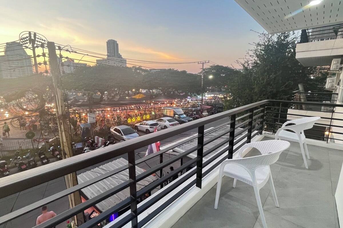 A balcony with white plastic chairs and a railing overlooking a busy street with cars and buildings.