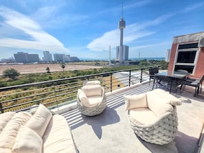 A rooftop terrace with cushioned seating and a table, overlooking a cityscape with modern buildings and a tower. - The Ocean Pearl Suites - Steps Pattaya Waterpark (Pattaya)
