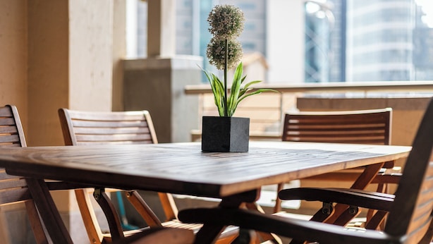 Une table en bois, ornée d’une plante en pot au centre, entourée de chaises en bois.