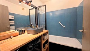 A bathroom with a wooden vanity, two sinks, a large mirror, a bathtub, and a blue-tiled wall. - Cozy apartment in Briançon, close to the slopes (Briançon)