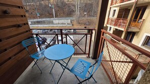 A balcony with a table and chairs, a view of parked cars, and a building with balconies. - Cozy apartment in Briançon, close to the slopes (Briançon)
