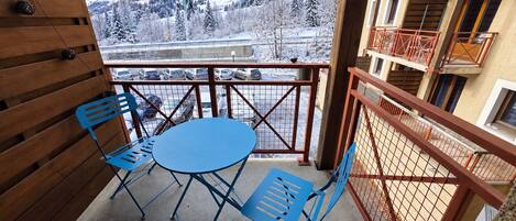Un balcone con tavolo e sedie, vista su montagne innevate e un'area di parcheggio.