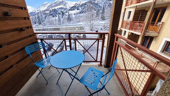 A balcony with a table and chairs, a view of snow-covered mountains, and a parking area.