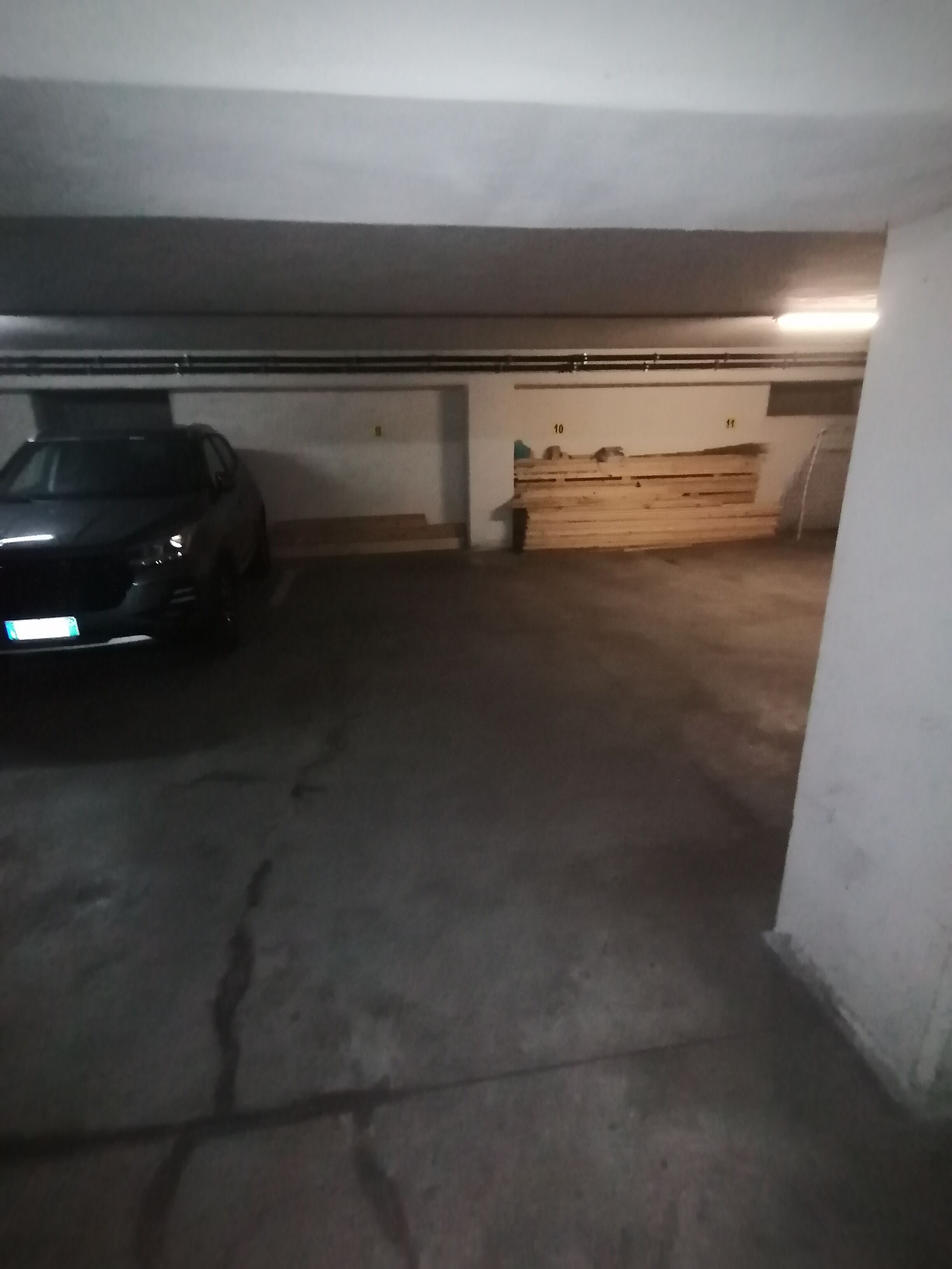 A dimly lit parking garage with a car parked in the left lane. The garage has concrete walls and a wooden bench in the center.