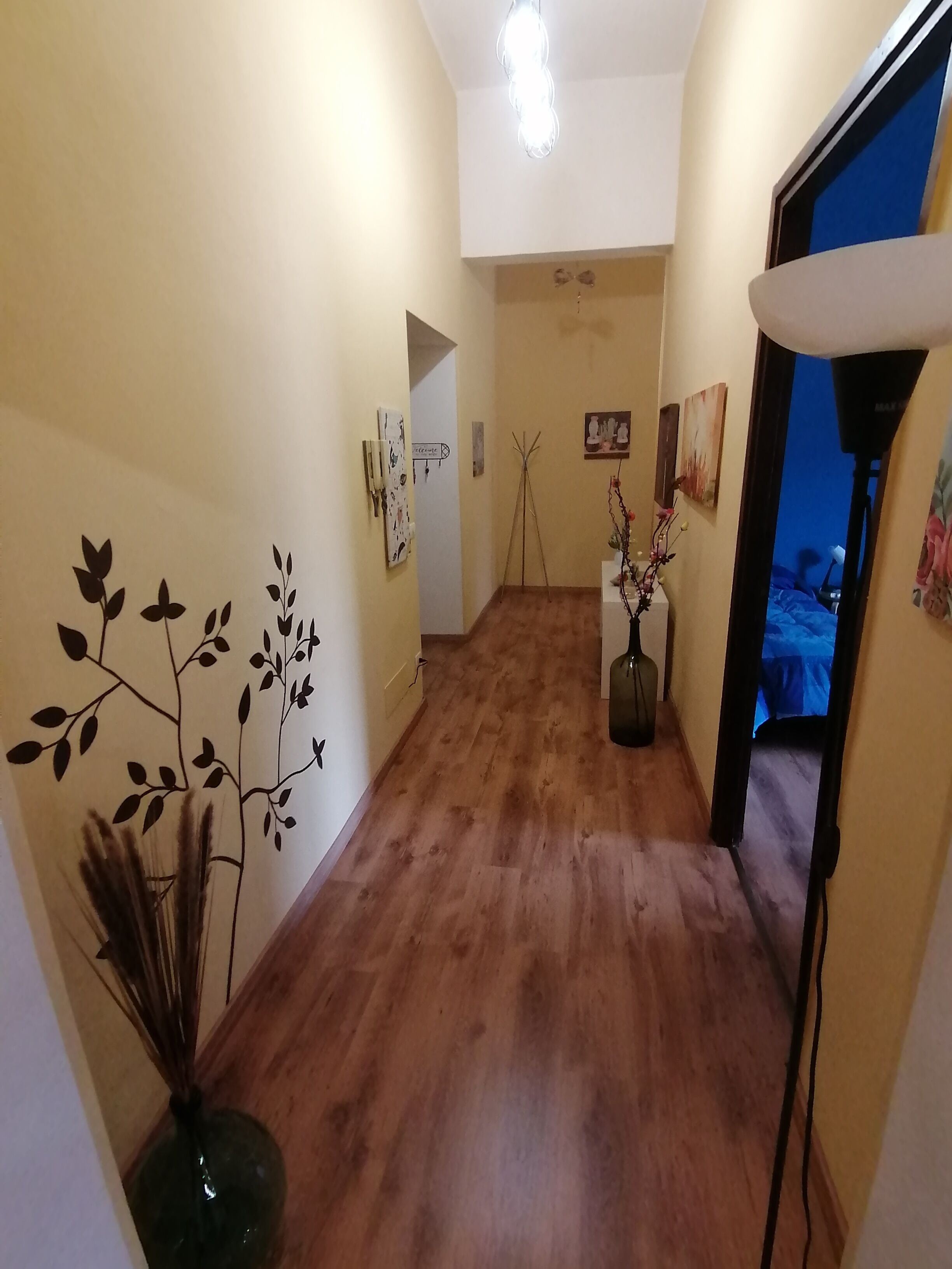 A hallway with wooden flooring, a vase with dried plants, and wall art.