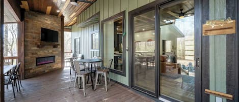 Une terrasse couverte avec un plancher en bois, une cheminée en pierre et un téléviseur fixé au mur.