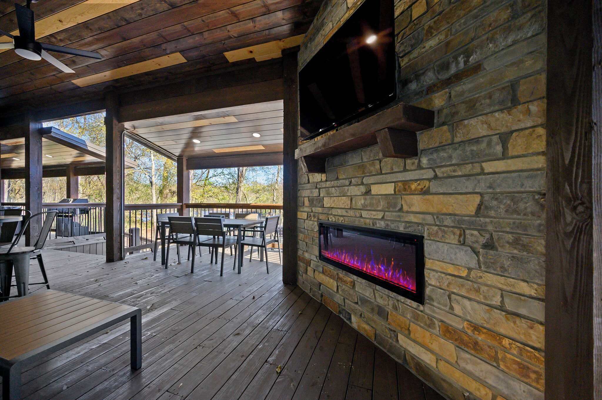 Un patio exterior con suelo de madera, paredes de piedra y chimenea integrada.