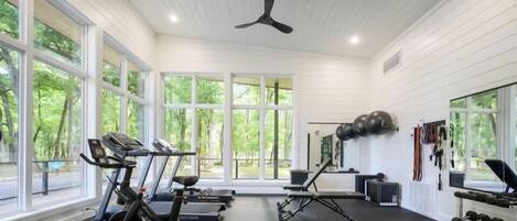 Een sportschool met trainingsapparatuur, grote ramen en een plafondventilator.