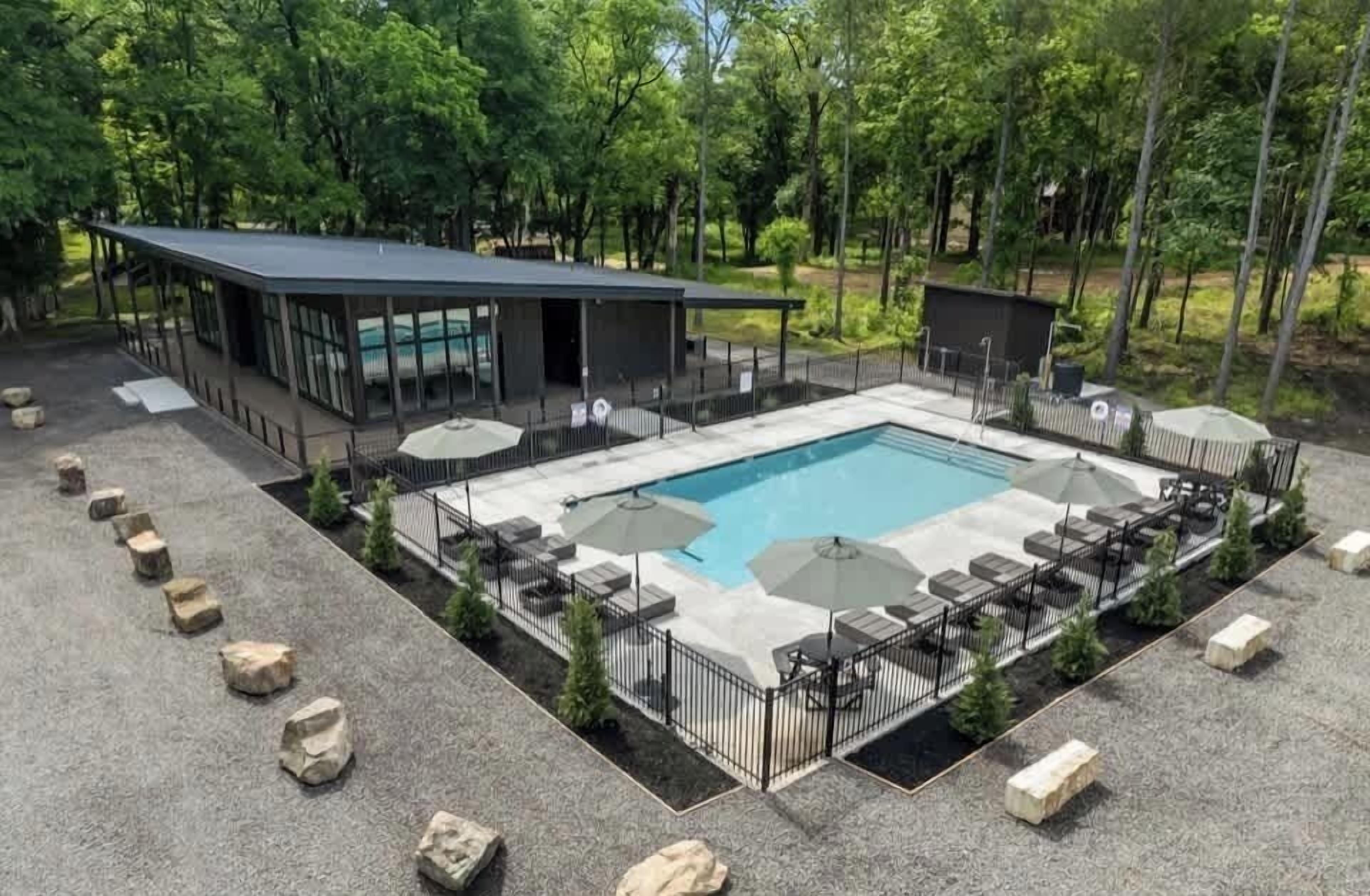 A modern outdoor pool area with lounge chairs and umbrellas, surrounded by a stone deck and a building with large windows.