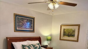 Una cama bien hecha con ropa blanca y un cojín verde, un cabecero de madera y un ventilador de techo con luz.