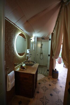 Een badkamer met een ronde spiegel, een wastafel, een douche en vloertegels met een patroon.