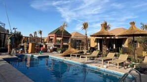 Une piscine entourée de palmiers et d’immeubles, avec des chaises longues et des parasols.