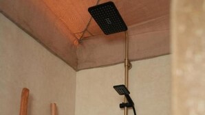 Une douche équipée d’un pommeau de douche à main et d’un flexible, d’une échelle en bois et d’un plafond texturé.