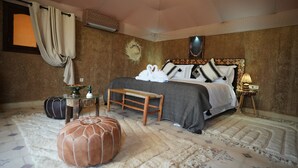 A bedroom with a bed, a bench, a small table, a pouf, and a wall-mounted lamp. - Deluxe family suite with private pool  in agafay (Agafay)