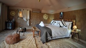 Une chambre à coucher avec un lit, une petite table, une chaise, une lampe et un ventilateur fixé au mur.