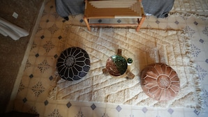 Un lit avec une couverture grise et deux oreillers, un tabouret en bois et un tapis à motifs.
