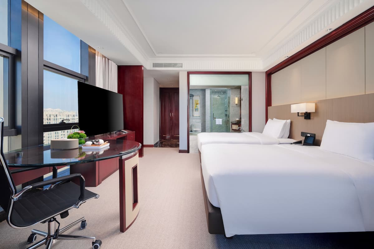 Una habitación de hotel con escritorio, dos camas, televisor y vista a la ciudad.