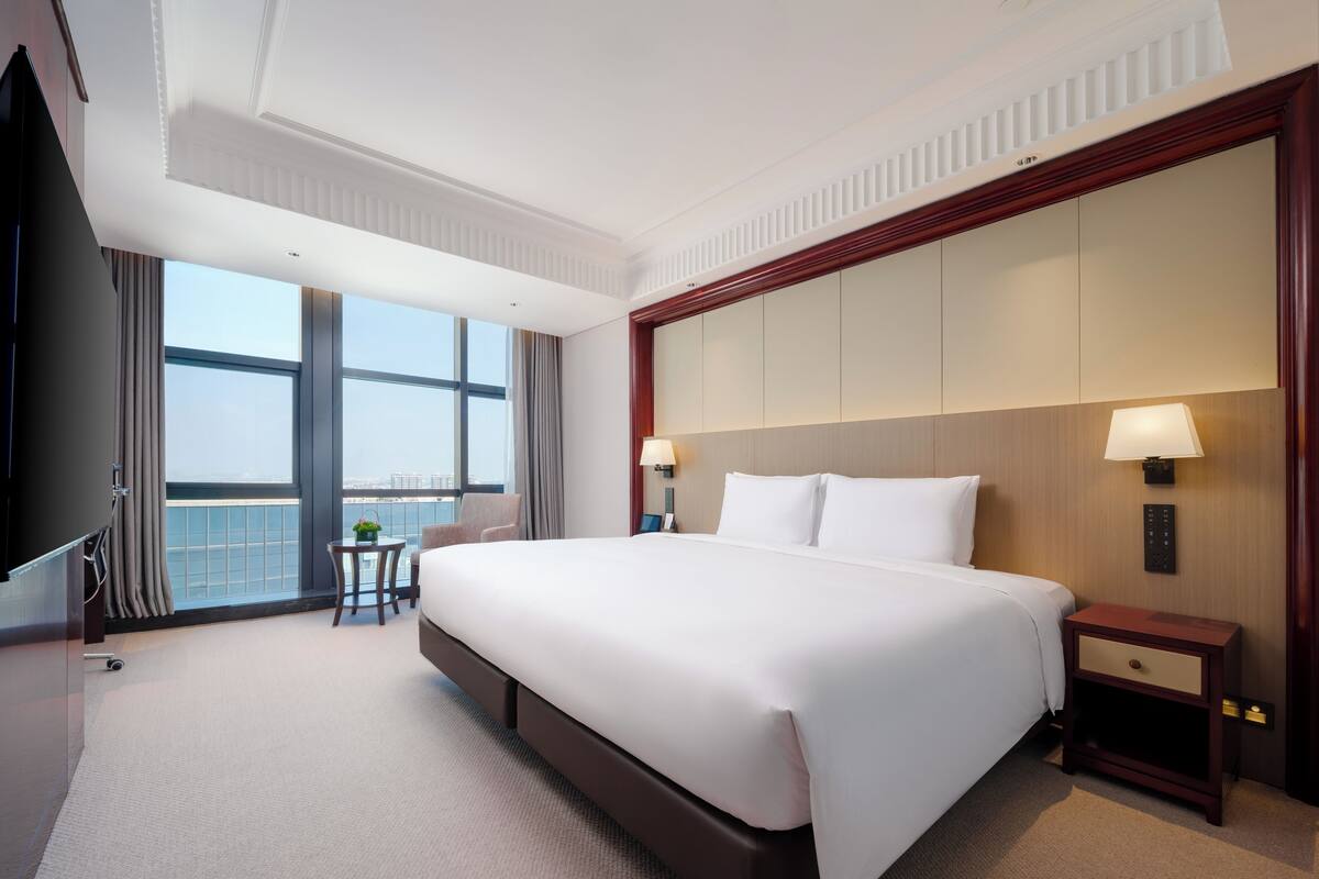 Habitación de hotel con una cama grande, una mesita de noche, un escritorio con silla, un televisor y una ventana con vistas.