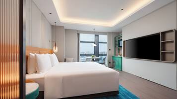 Habitación de hotel moderna con una cama grande, zona de comedor, televisor y vistas a la ciudad.