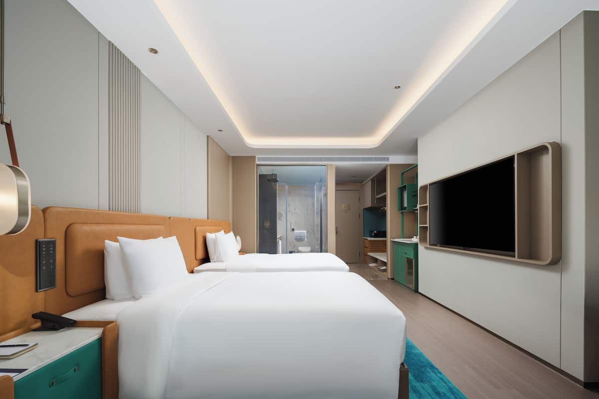 Una habitación de hotel moderna con dos camas, televisión, baño y vestidor.
