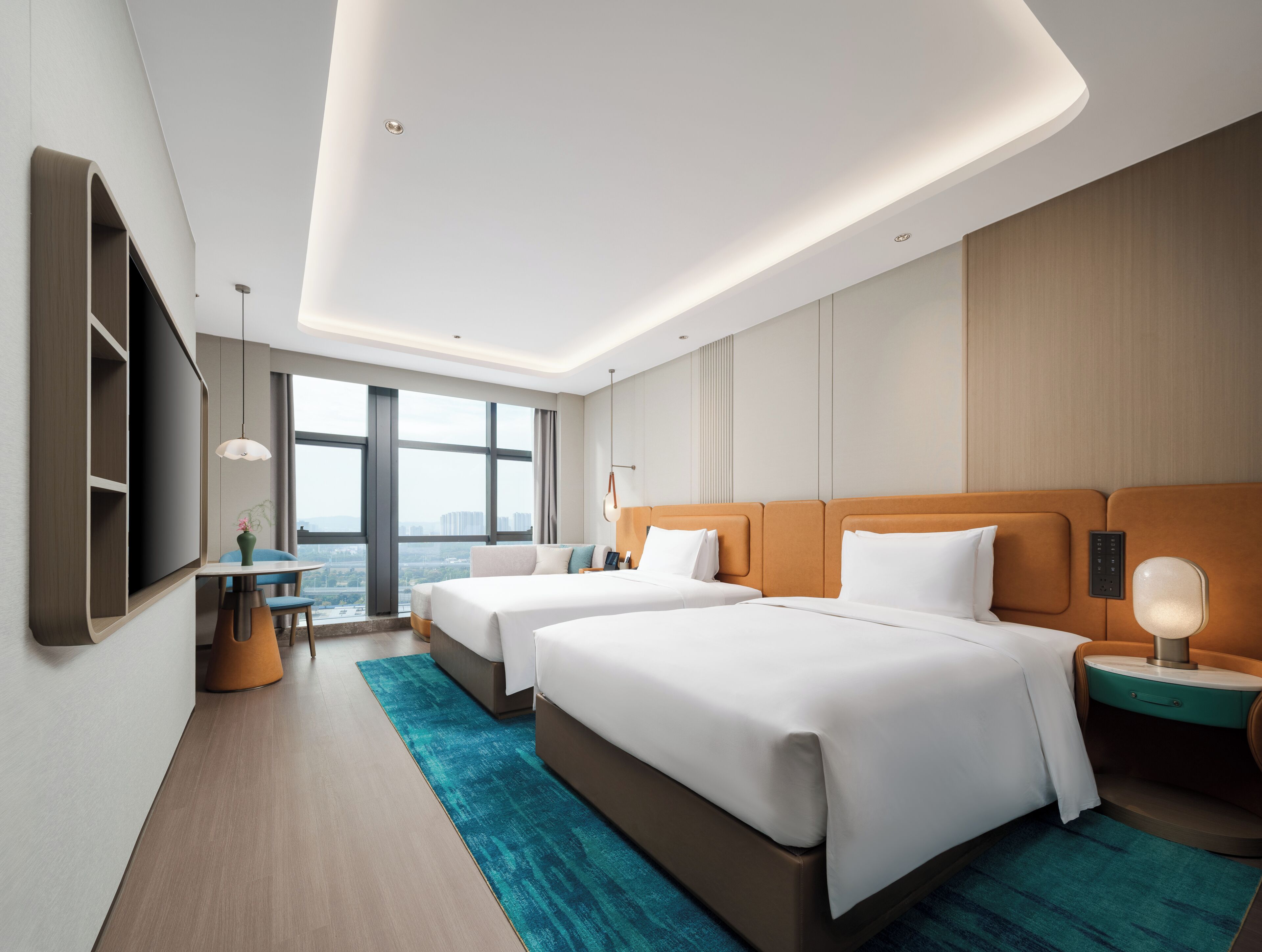 A modern hotel room with two beds, a TV, a desk, and a large window offering a city view.
