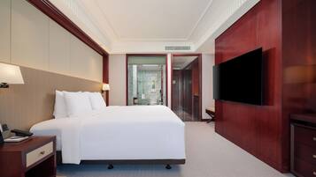 Habitación de hotel con una cama grande, mesitas de noche, televisión y baño visible a través de un cristal.