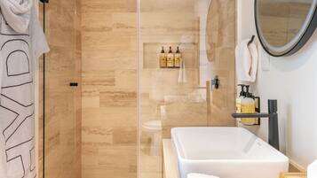 Un baño moderno con ducha de vidrio, una bañera blanca grande y un tocador con artículos de aseo.