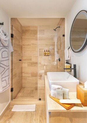 Een moderne badkamer met een douche met glazen wand, een ruim ligbad en een wastafel met toiletartikelen.
