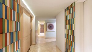 Un couloir aux murs ornés de motifs, une œuvre d’art encadrée accrochée au mur et une porte au fond.