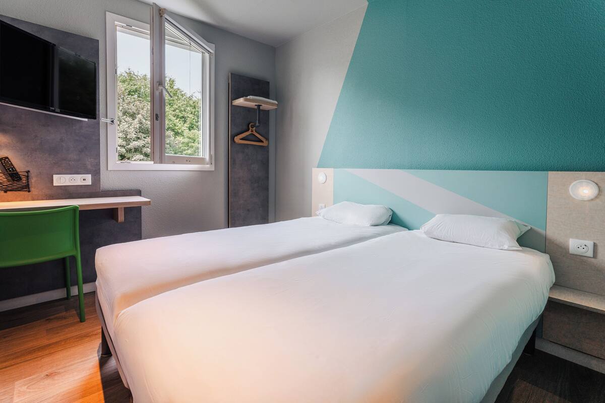 Une chambre d’hôtel moderne avec deux lits, un bureau et une fenêtre donnant sur la verdure.