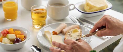 A breakfast table with a bowl of fruit, a plate with bread and butter, a cup of coffee, and a glass of juice.