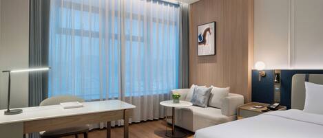 Habitación de hotel moderna con escritorio, sofá, cama y una pequeña mesa con una planta.
