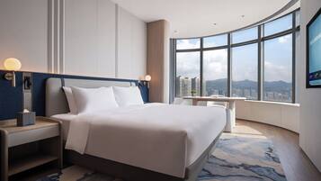 Habitación de hotel moderna con una cama grande, mesitas de noche, un escritorio y un amplio ventanal con vistas a la ciudad.