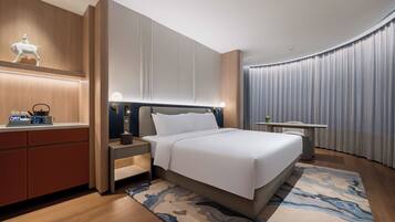 A modern hotel room with a large bed, bedside tables, a desk, and a decorative wall piece.