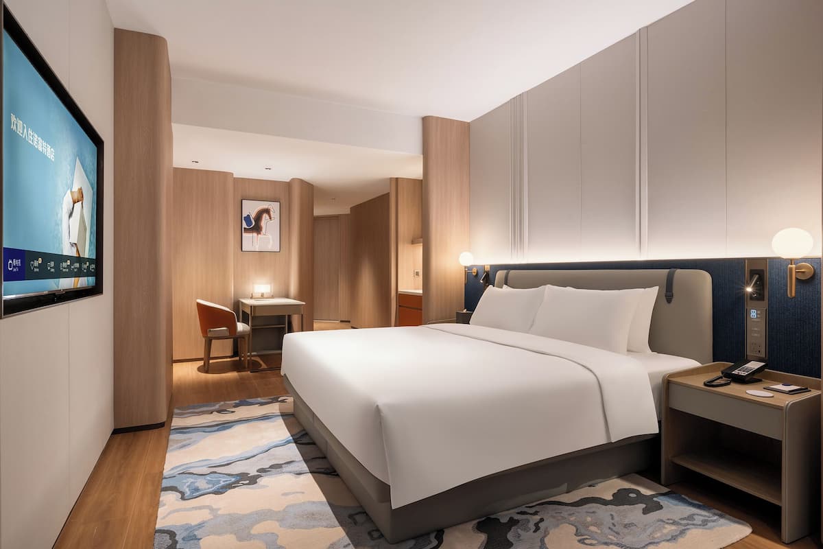 A modern hotel room with a large bed, bedside tables, a desk, and a TV mounted on the wall.