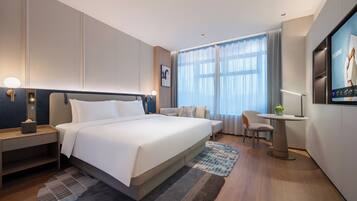 A modern hotel room with a large bed, bedside tables, a desk, and a TV.