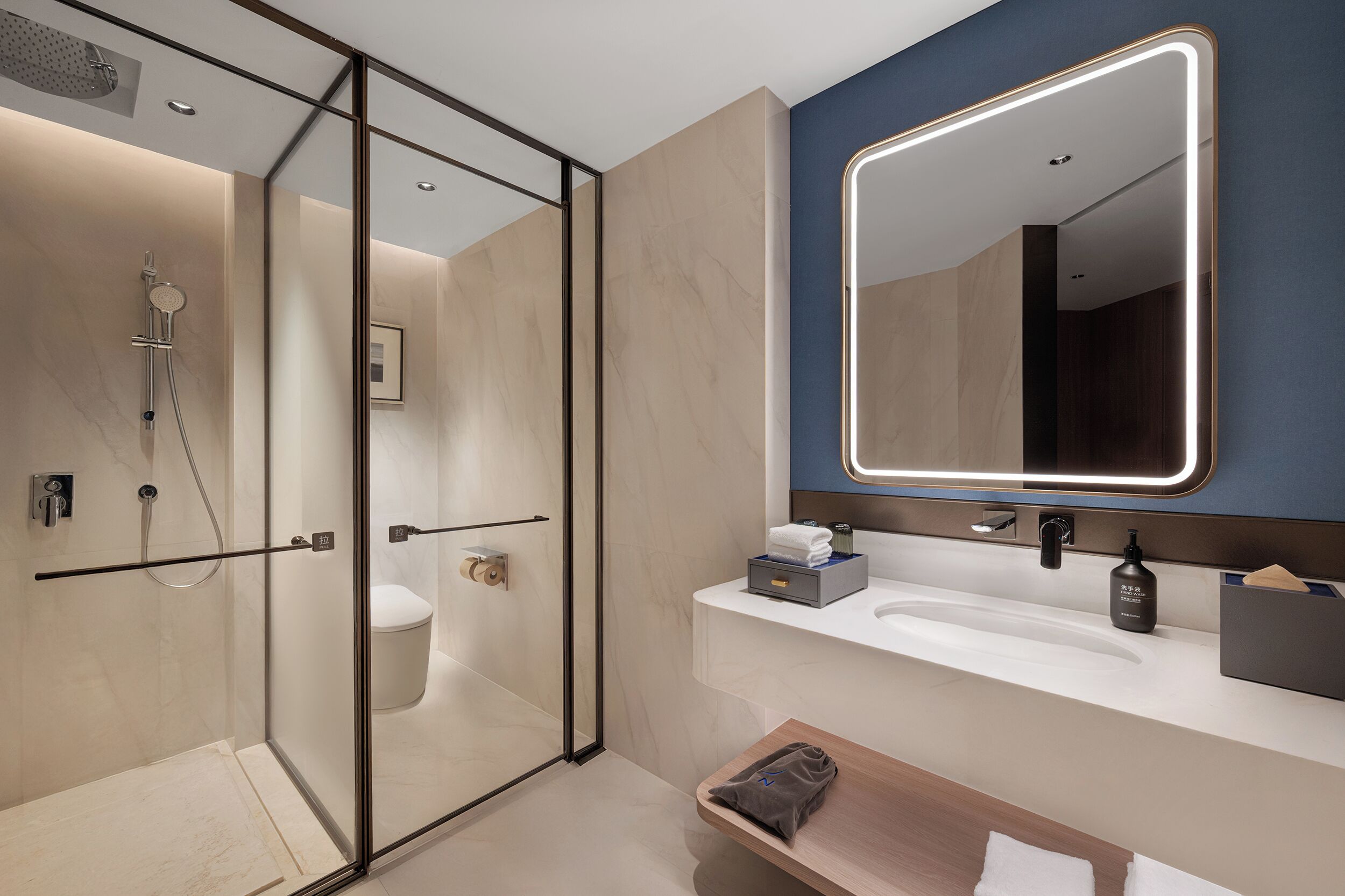 A modern bathroom with a glass-enclosed shower, a large mirror with LED lighting, a white sink, and a wooden vanity.