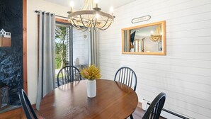 Ein Essbereich mit einem Holztisch, Stühlen, einer Chandelierleuchtre und einem Spiegel an der Wand.