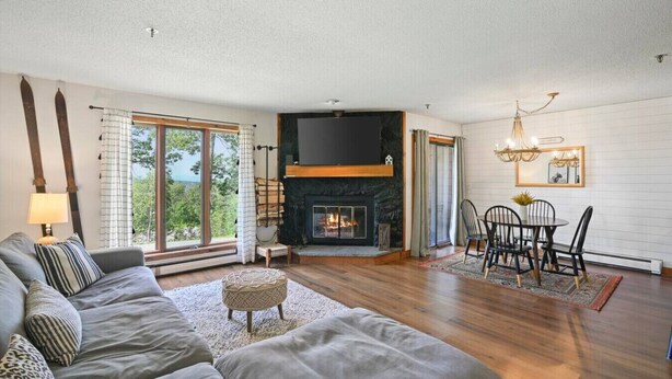 Ein Wohnzimmer mit Kamin, einer Couch, einem Esstisch mit Stühlen und einem großen Fenster mit Vorhängen.
