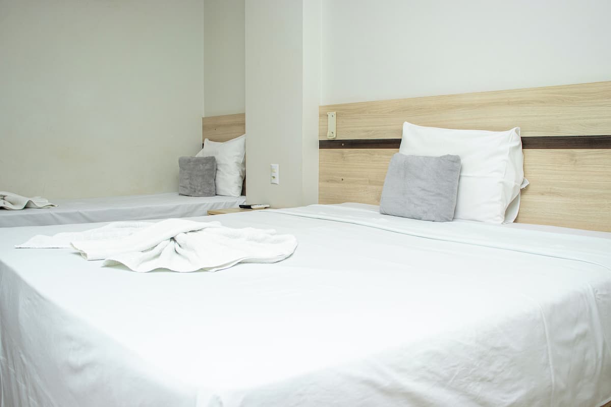 A hotel room with two beds, each with white linens and grey pillows.