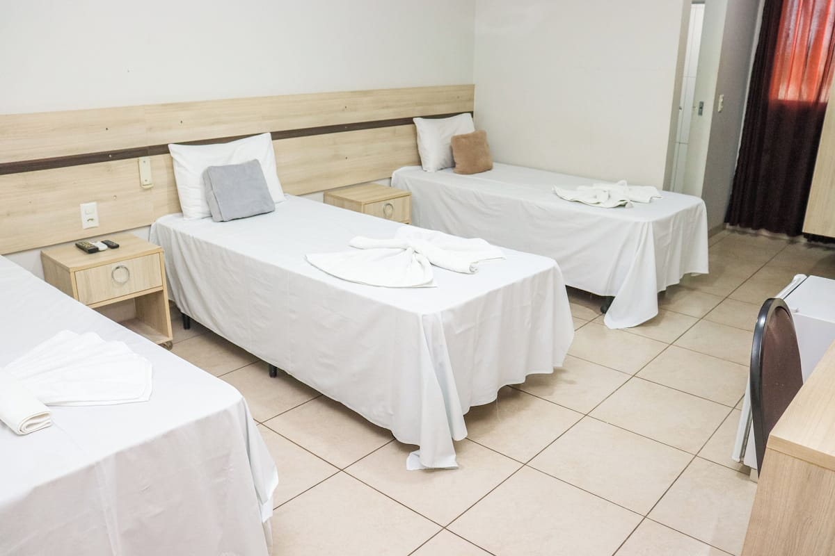 A hotel room with two single beds, each with a wooden headboard, white bedding, and a small bedside table with a lamp.