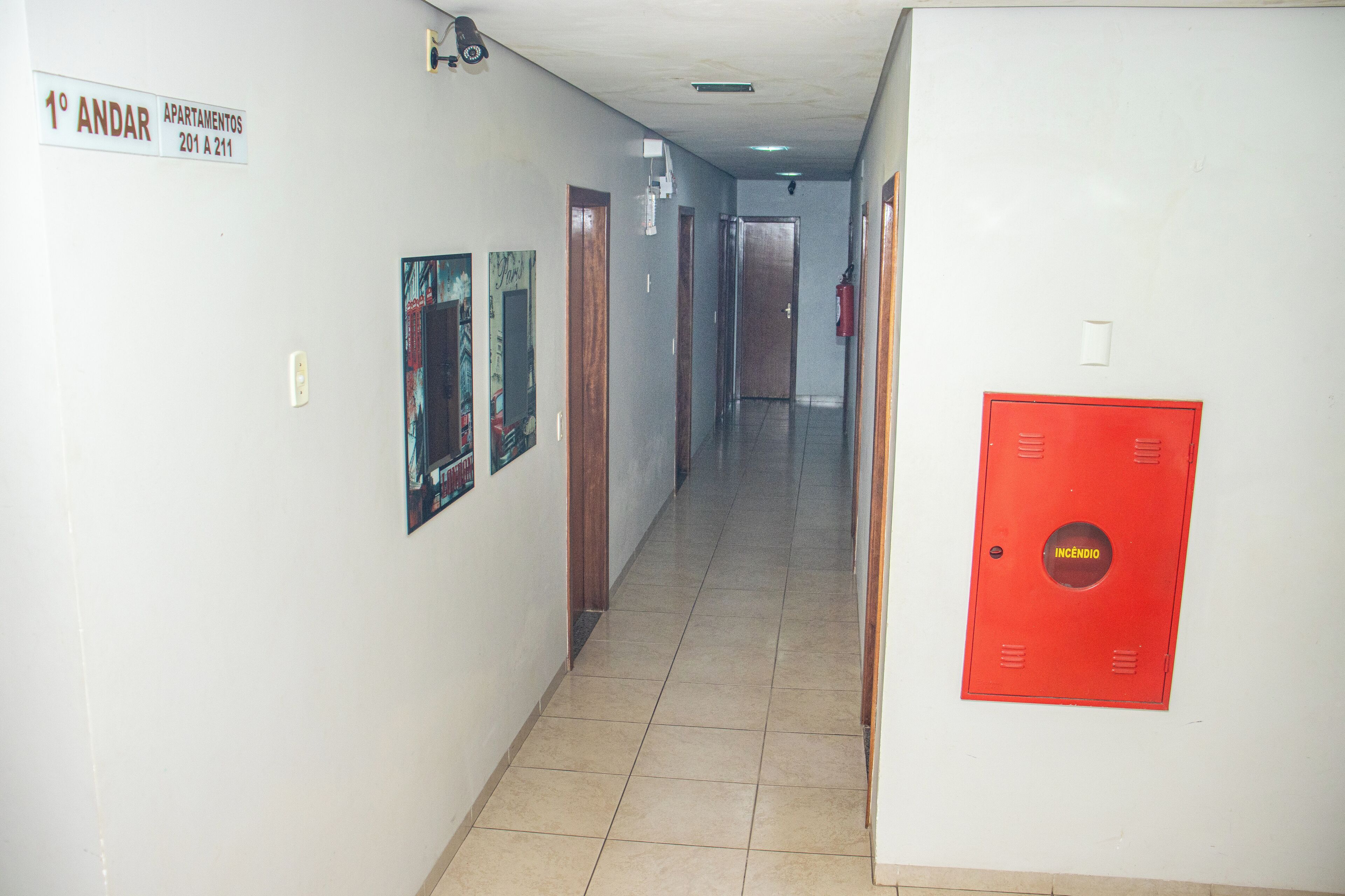 A hallway with a fire extinguisher, a sign indicating apartments 201 to 211, and a red emergency exit sign.