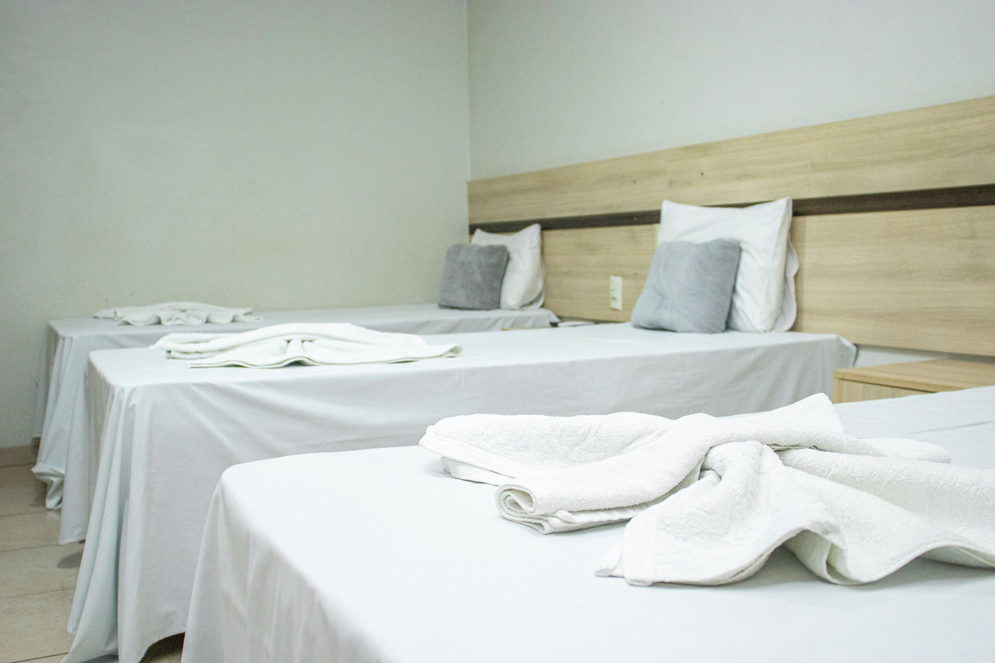 Quarto de hotel com duas camas individuais, cada uma com colcha branca e um travesseiro.