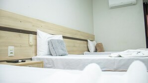 A hotel room with two beds, a wooden headboard, white bedding, a remote control, and an air conditioning unit. - Foavi Hotel (Araguaína)