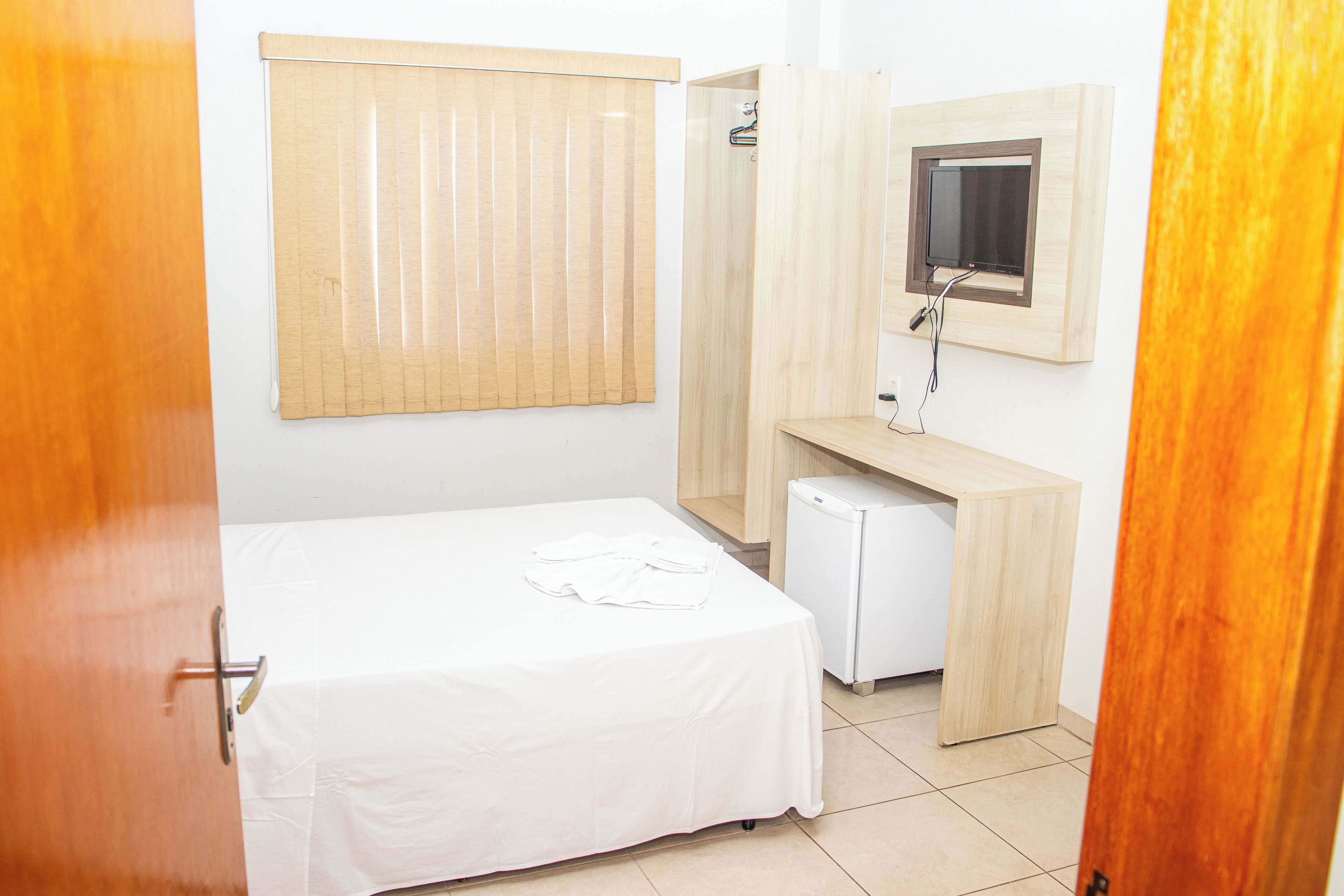 A bedroom with a bed, a small desk, a mirror, and a television.