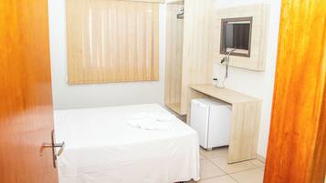 A bedroom with a bed, a small desk, a mirror, and a television.