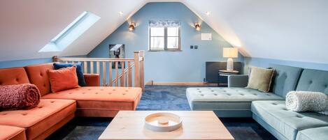 Un dormitorio de ático acogedor con techo inclinado, un tragaluz, una escalera de madera, un ventanal grande y una cama con cabecera.
