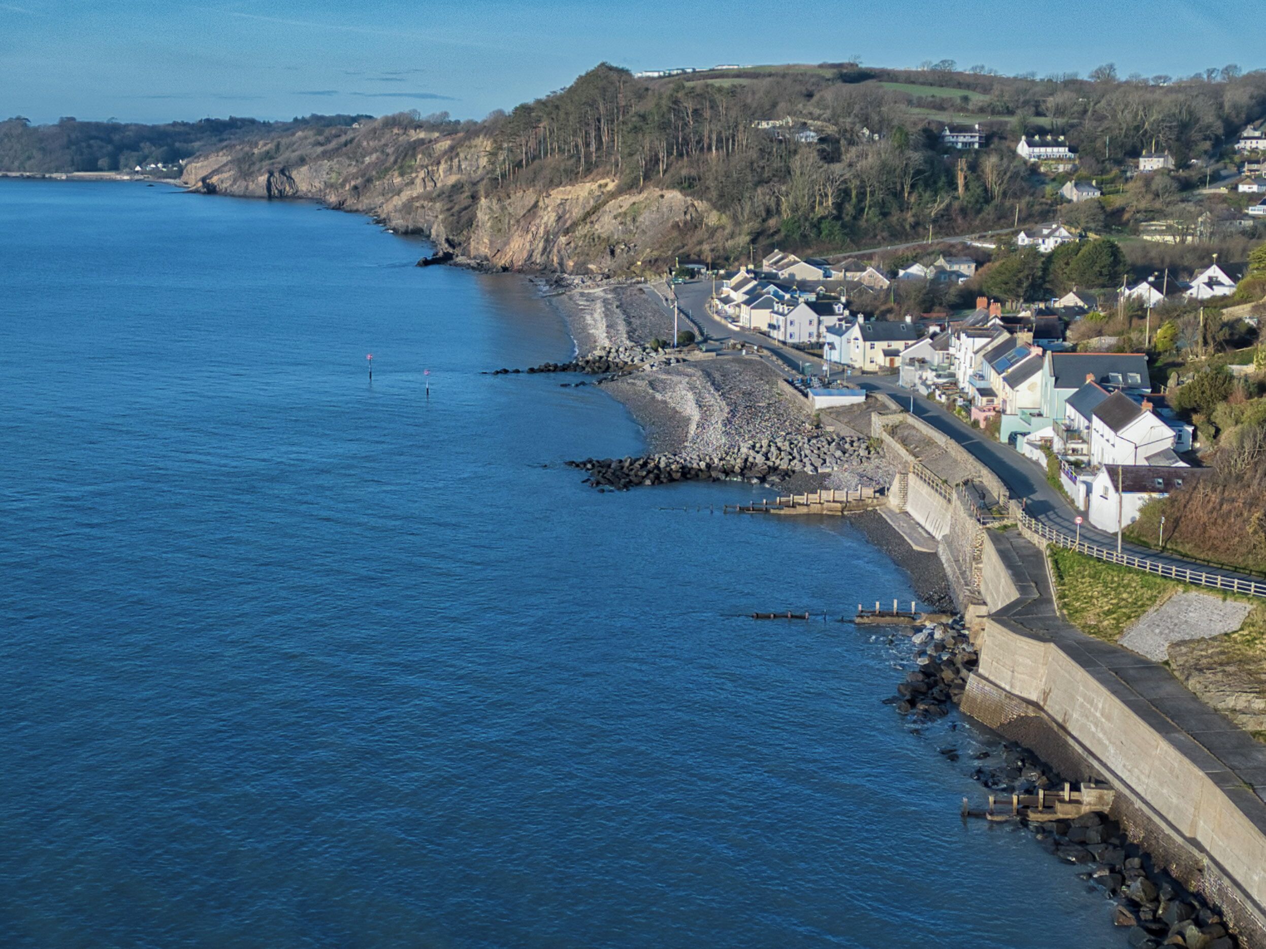 A coastal town with houses along the shore, a rocky breakwater, and a clear view of the sea.