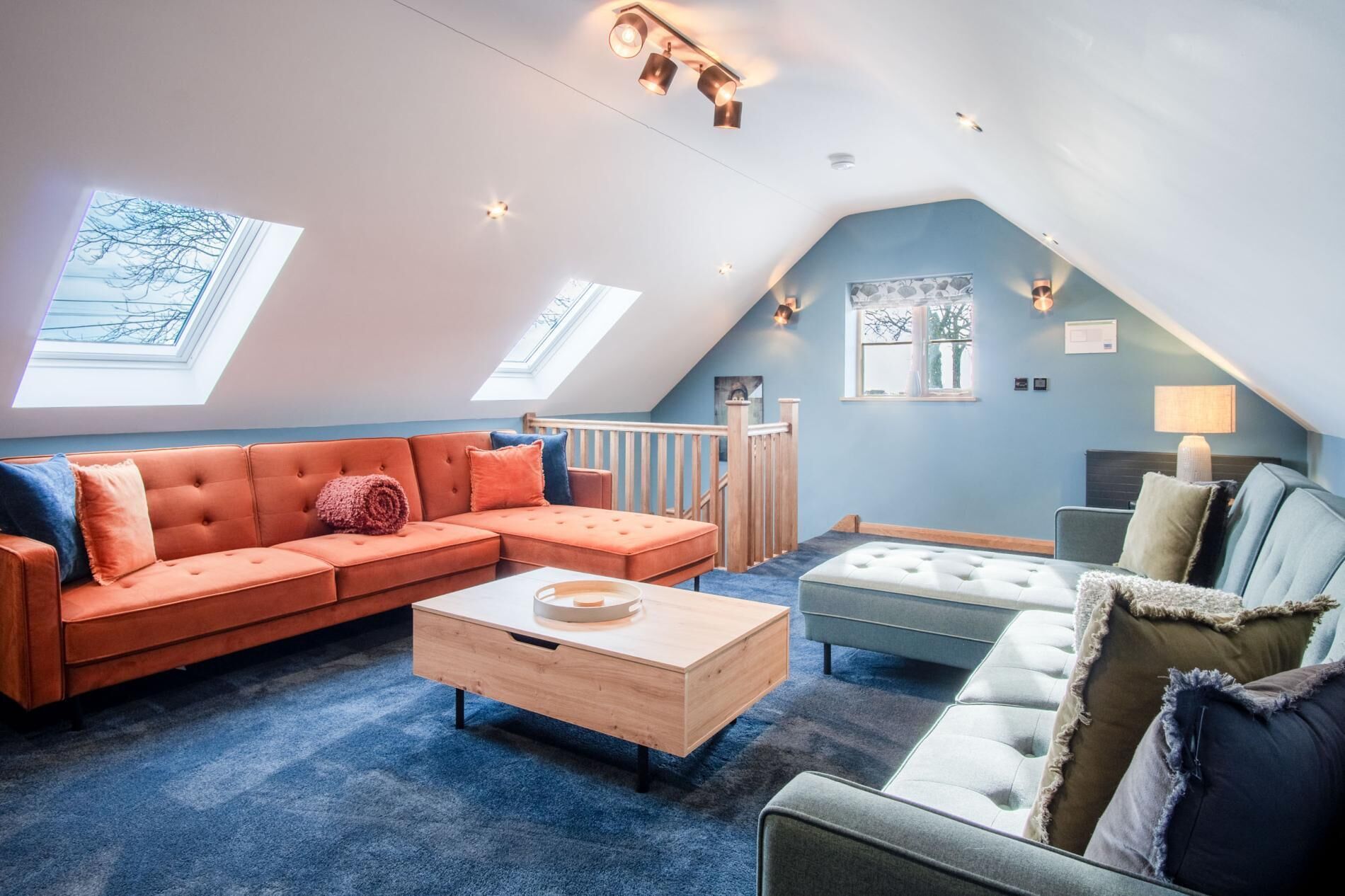 Ett ombonat vardagsrum i loftstil med en stor, orange soffa, en ljusblå fåtölj och ett soffbord i trä.